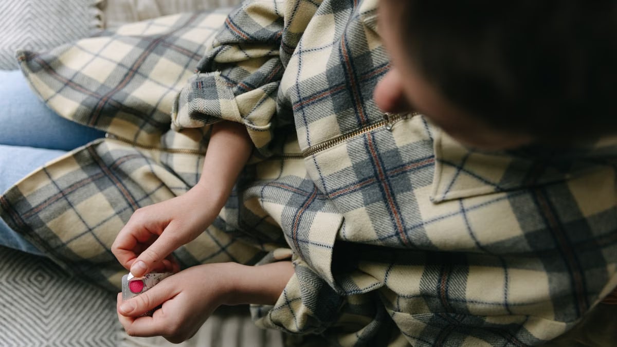 Close-up of hands opening a blister pack while sitting on a sofa with a plaid shirt, indoors.