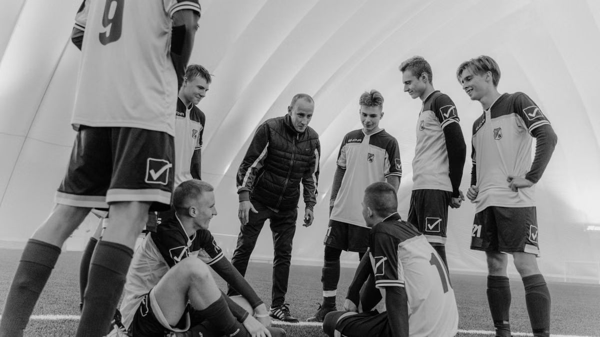Black and white photo of soccer team and coach planning strategy indoors.